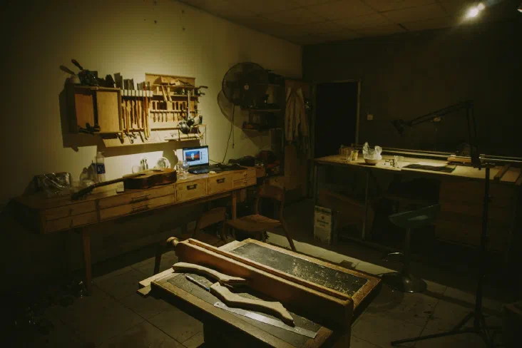 A dark workshop filled with hand tools hanging on a pegboard and wood pieces on a workbench