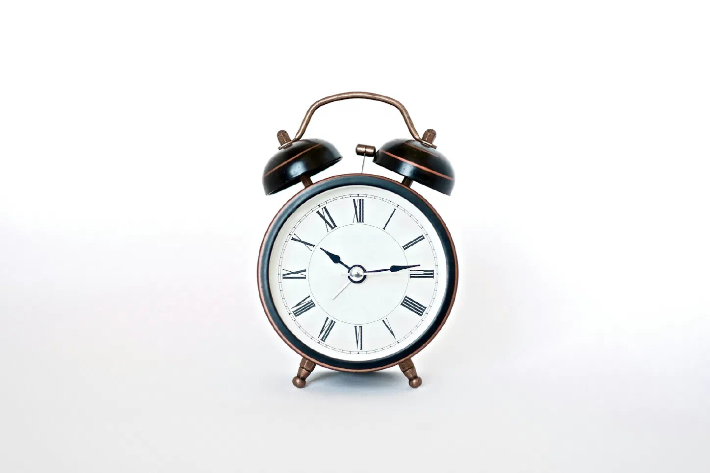 A vintage twin-bell alarm clock with Roman numerals on a plain white background