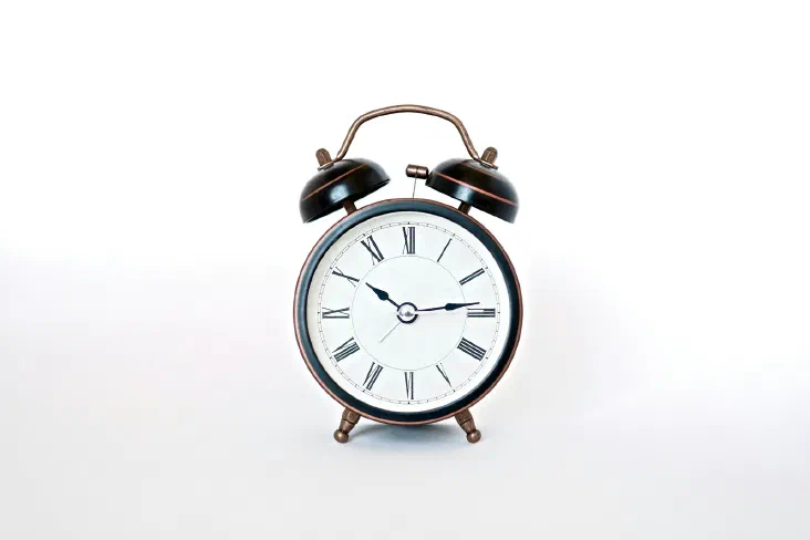 A vintage twin-bell alarm clock with Roman numerals on a plain white background