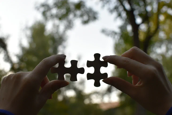 A person's hands holding two puzzle pieces together, about to connect them