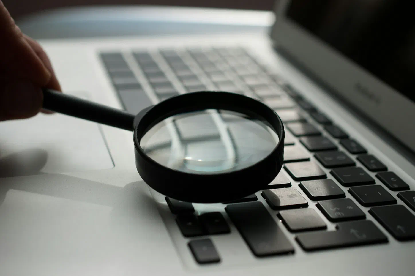 A magnifying glass resting beside a gray laptop computer