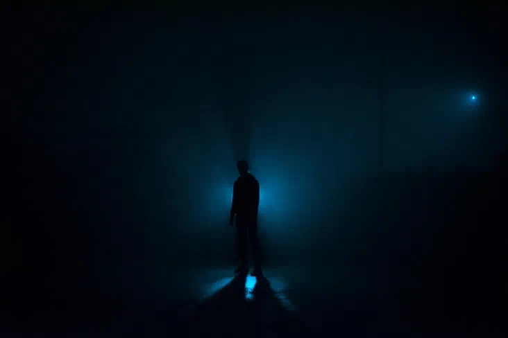 A person standing in darkness holding a lit flashlight, its beam cutting through the black