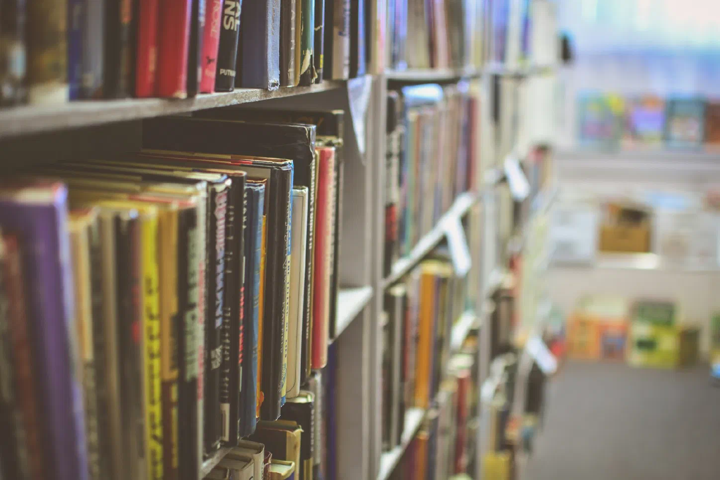 Close-up of library bookshelves packed with books, shot at an angle down the row with the far end of the aisle blurred